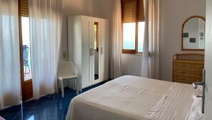 Ein Schlafzimmer mit einem Bett, einem Kleiderschrank, einem Stuhl, einem Fenster mit Jalousien und einem Spiegel an der Wand.