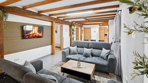 Una sala de estar moderna con chimenea, sofás grises, una mesa de centro de madera y vigas de madera a la vista.