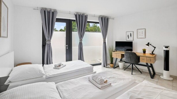 Habitación de hotel con dos camas, un escritorio con computadora, un televisor y una ventana con cortinas.