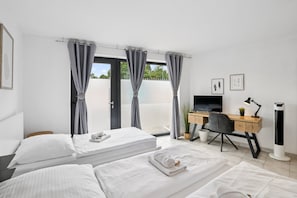 A hotel room with two beds, a desk with a computer, a TV, and a window with curtains.