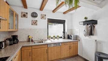 A kitchen with wooden cabinets, a built-in dishwasher, a coffee maker, and a window with plants.