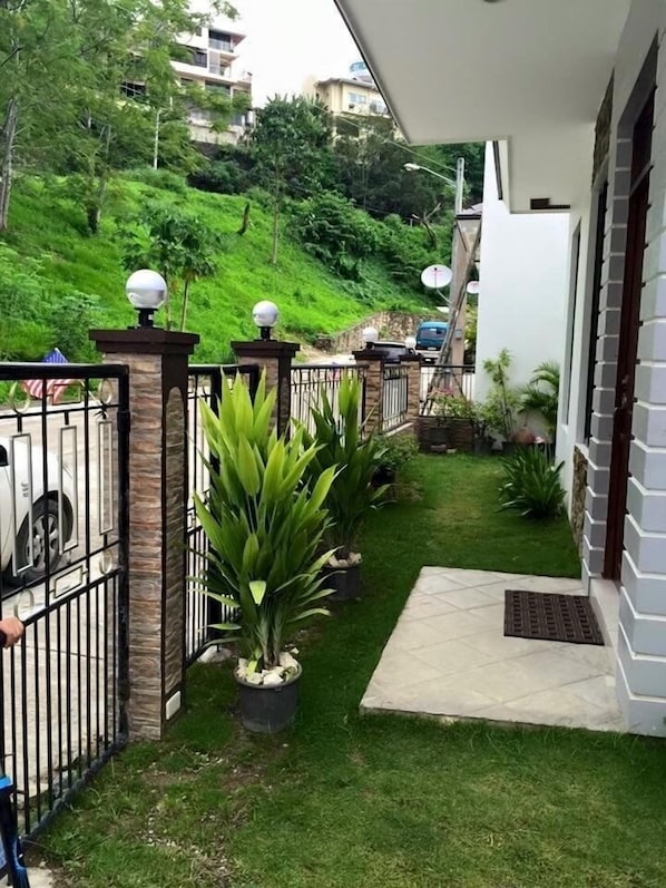 A gated entrance with a small lawn, potted plants, and a white building with a balcony.