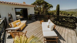 A wooden deck with outdoor seating, a small building with a tiled roof, and a view of trees and hills.