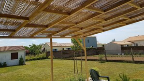 A covered outdoor area with a wooden structure, a chair, and a grassy lawn. - House with enclosed garden, on the sea side (Brem-sur-Mer)