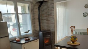 A modern kitchen with a brick wall, a black stove, and a dining area with a table and chairs. - House with enclosed garden, on the sea side (Brem-sur-Mer)