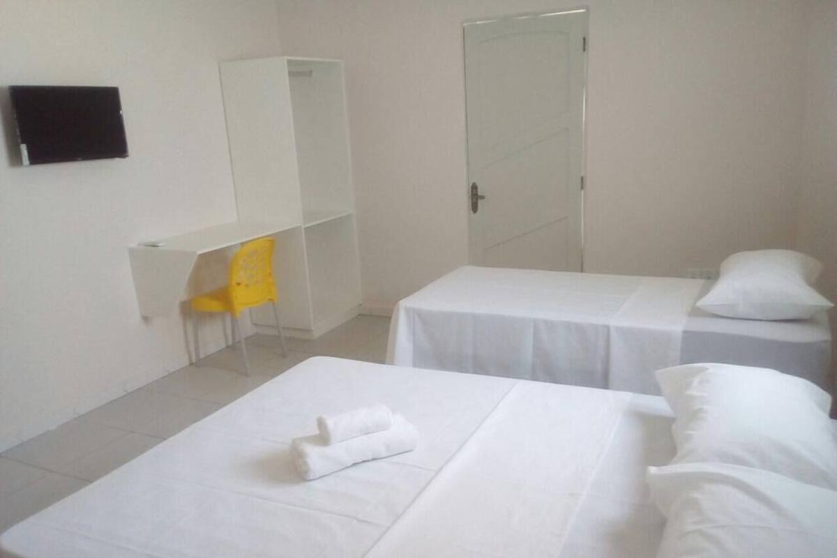A hotel room with two single beds, a chair, a desk, and a door.