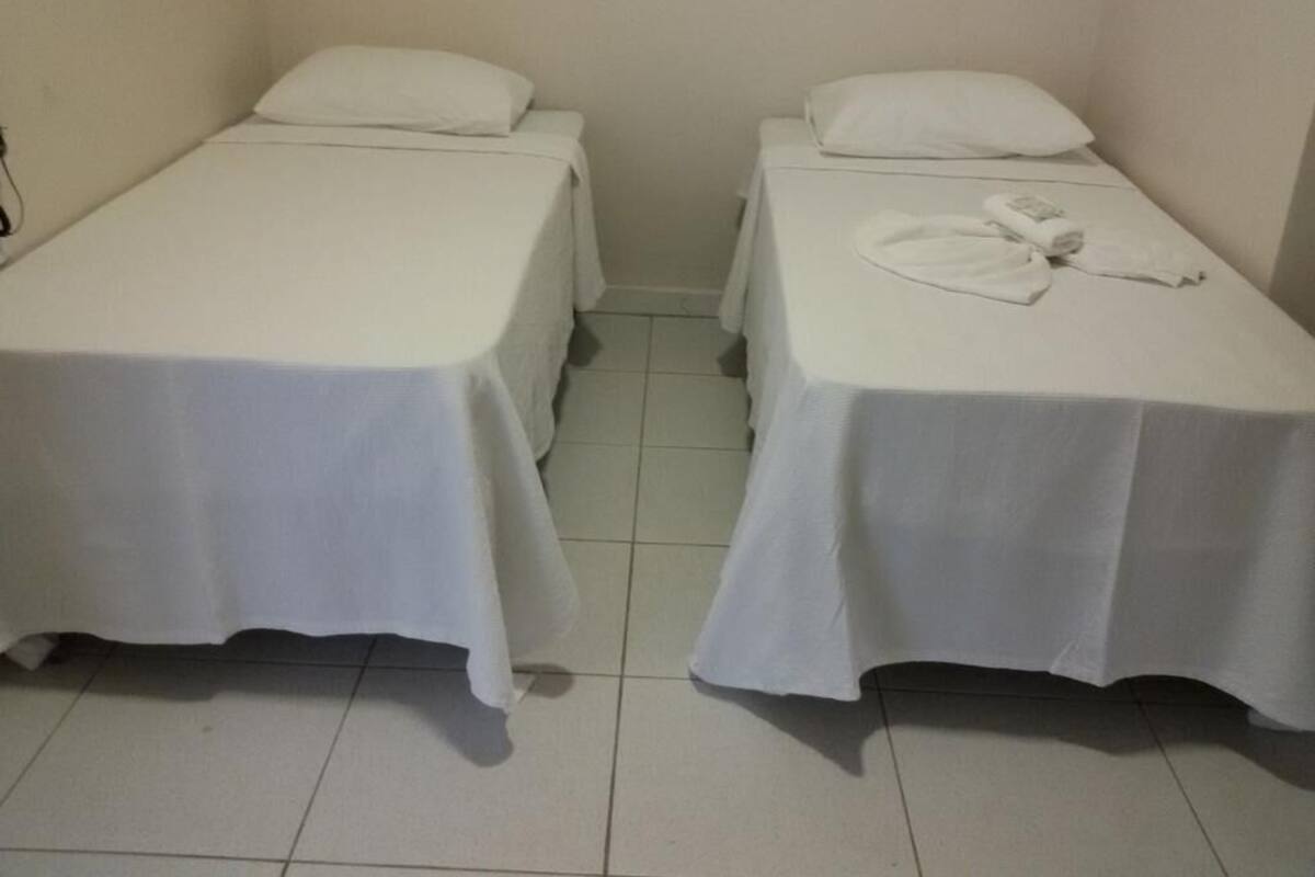 Two single beds with white linens in a room with tiled flooring.