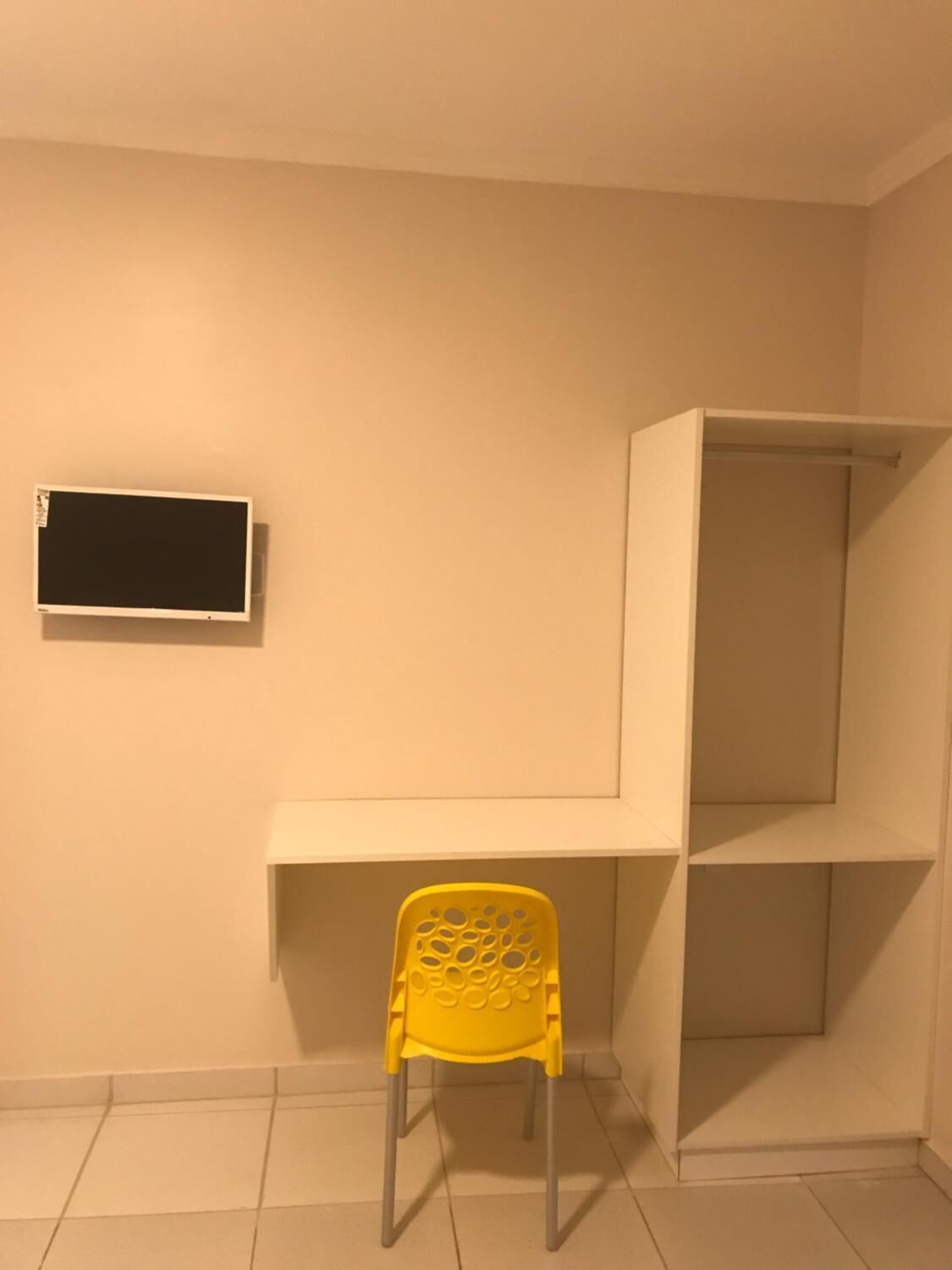 A room with a yellow chair, a white shelf, and a flat-screen TV mounted on the wall.