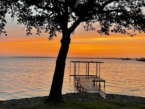 A sunset view over a calm body of water with a wooden pier and a gazebo.