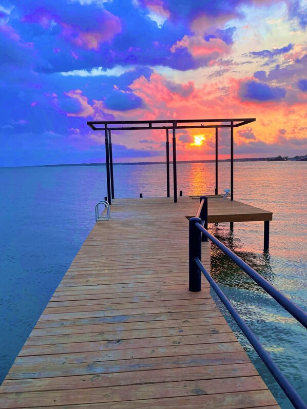 A wooden pier extending into calm water with a sunset in the background.