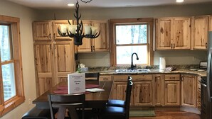 A kitchen with wooden cabinets, a dining table with chairs, a chandelier, and a window. - 3BR Cottage Nestled in a Door County Serene Setting (Sturgeon Bay)