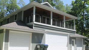 A two-story house with a garage, a balcony, and two trash bins. - 3BR Cottage Nestled in a Door County Serene Setting (Sturgeon Bay)