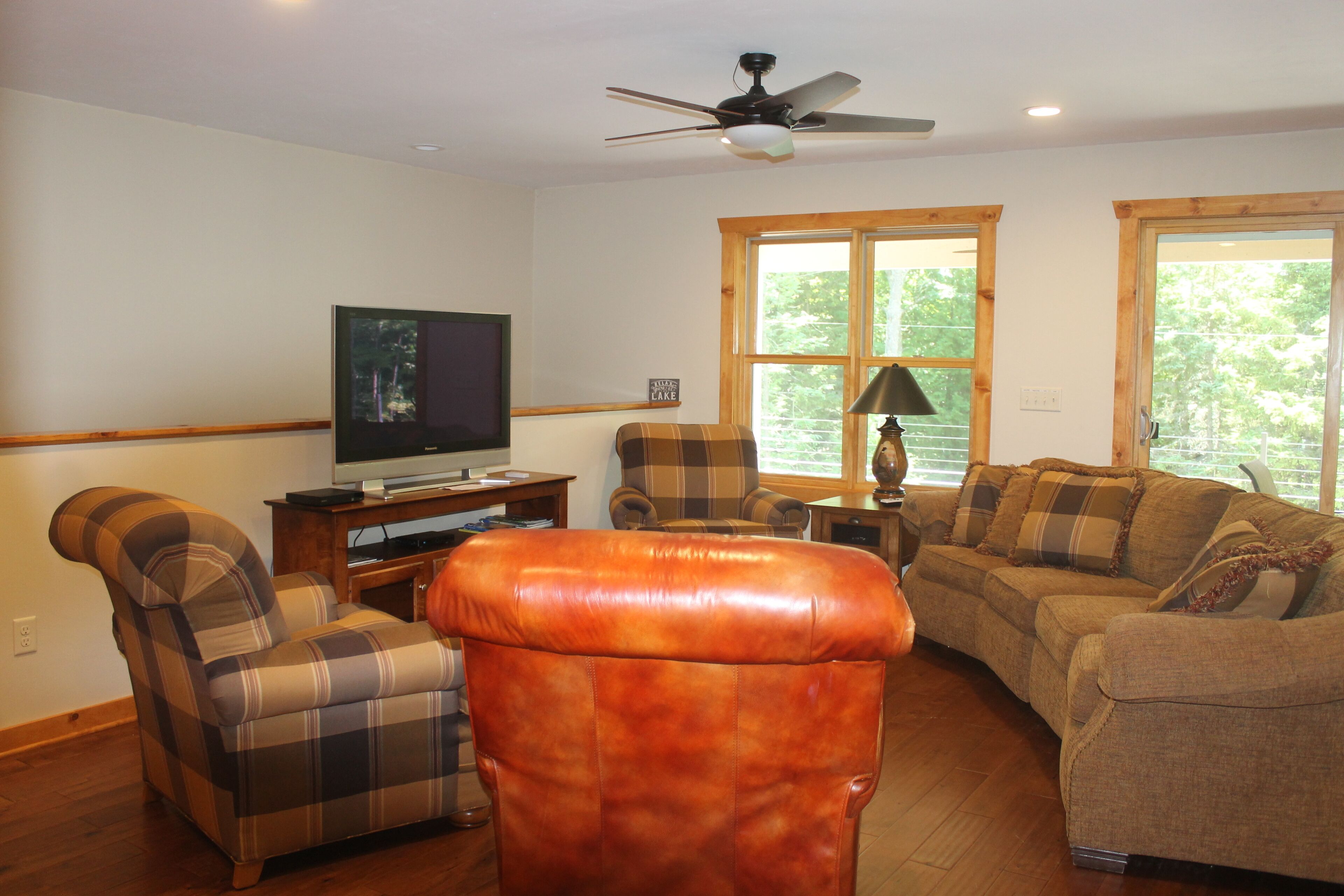 A living room with a television, two armchairs, a sofa, and a ceiling fan.