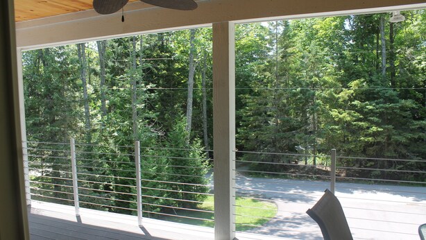 A covered outdoor area with a view of a forested area through large windows. - 3BR Cottage Nestled in a Door County Serene Setting (Sturgeon Bay)