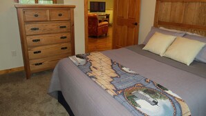 A bedroom with a bed, a wooden dresser, a door leading to another room, and a ceiling fan. - 3BR Cottage Nestled in a Door County Serene Setting (Sturgeon Bay)