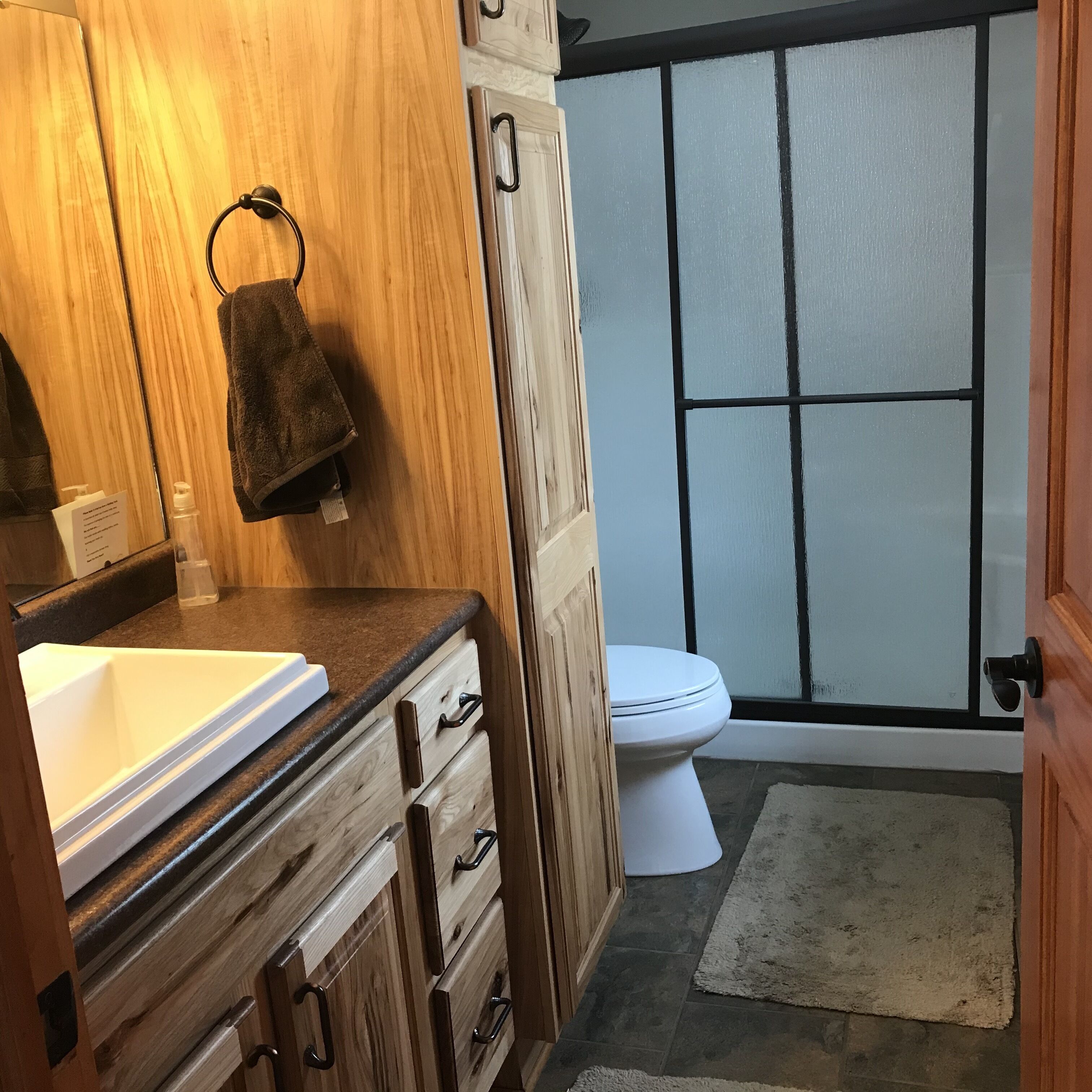 A bathroom with a wooden vanity, a white sink, a towel, a toilet, and a frosted glass shower door.
