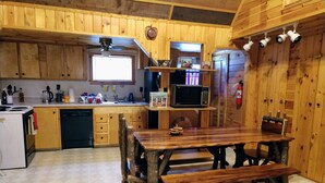 A rustic kitchen with wooden cabinets, a built-in microwave, and a wooden dining table with benches.