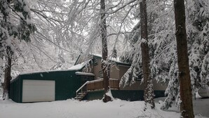 A snow-covered residential area with a garage, a wooden deck, and a house with a green roof.