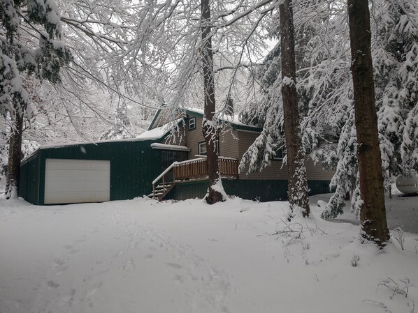 A snow-covered residential area with a garage, a wooden deck, and a house with a green roof.