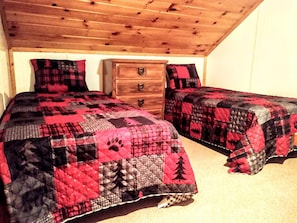 Une chambre avec deux lits, une commode en bois et un plafond avec des poutres apparentes.