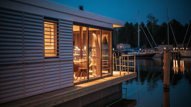 Ett hus vid vattnet med en inglasad veranda, en matplats och utsikt över båtar i bakgrunden.
