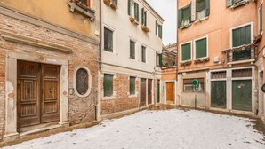A narrow alley with snow-covered ground, brick and plaster buildings, and wooden doors.