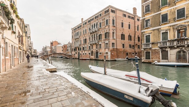 A canal with boats docked, historic buildings, and a pedestrian walkway.