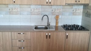 A kitchen with wooden cabinets, a stainless steel sink, a gas stove, and a backsplash with patterned tiles. - Saburtalo flat - Comfort created for you! (Tbilsi)