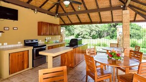 Cocina exterior cubierta con comedor, que incluye una mesa, sillas, ventilador de techo y vistas al entorno natural.