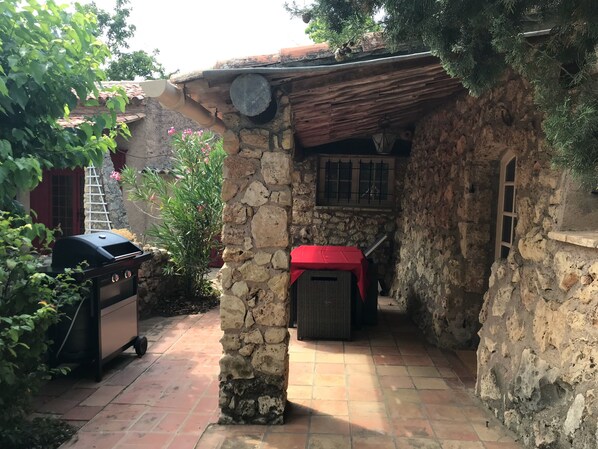 A stone-walled outdoor area with a grill, a red table, and a window with bars. - Petite Bergerie du Bouillidou (Cotignac)