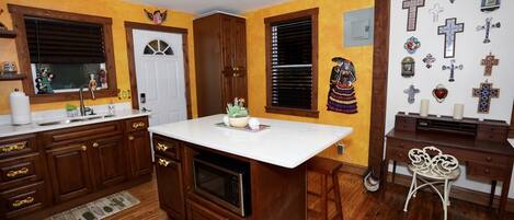 A kitchen with wooden cabinets, a white countertop, and a built-in microwave. There is a small island with a plant and a decorative item.