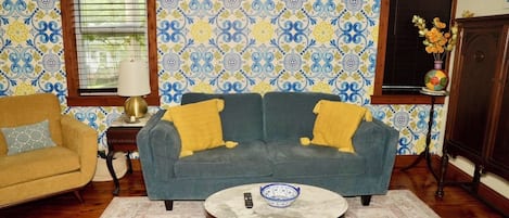 Ein Wohnzimmer mit blauem Sofa, gelben Kissen, einem runden Couchtisch und strukturierten Tapeten.