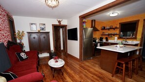 A living room with a red sofa, a small round table, and a kitchen area with a refrigerator and wooden cabinets. - HistoricHotspot! walk to bars, resturaunts, shops. GREAT NIGHTLIFE! Pet Friendly (Jacksonville)
