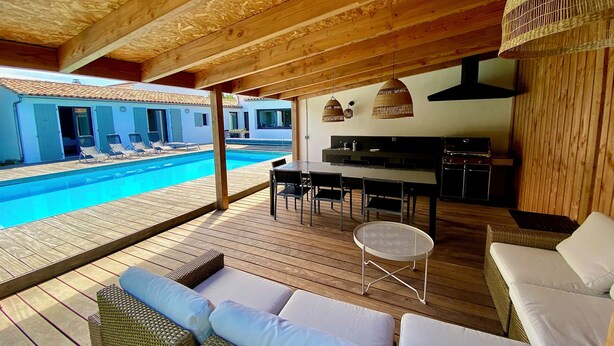 Une terrasse en bois avec une piscine, un espace salon extérieur et un coin cuisine.