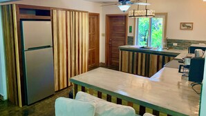 Eine kompakte Küche mit integriertem Kühlschrank, Holzvertäfelung, einem Esstisch mit Stühlen, einem Deckenventilator und einem Fenster mit Blick ins Grüne.