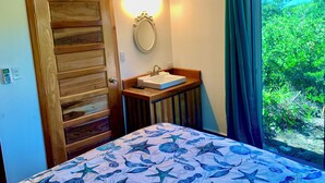 Ein Schlafzimmer mit Holztür, einem Nachttisch mit Spüle, einem Spiegel und einem Bett mit Bettdecke im Sterndruck.