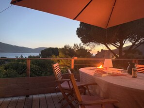 A wooden deck with a table and chairs, overlooking a body of water and hills. - CORSICA - AJACCIO Charming villa with ocean views, 100 meters from the beach (APPIETTO)