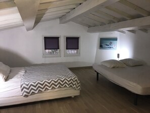 Ein Schlafzimmer mit zwei Betten, Holzbalken an der Decke und zwei mit Vorhängen versehenen Fenstern.