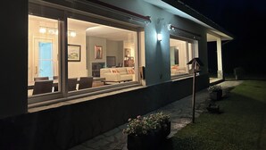 A modern house with large windows, a visible living room with a sofa and TV, and a well-lit exterior. - VILLA LOUISE BILBAO, IN A GREEN SETTING, CLOSE TO THE CITY AND BEACHES (Berango)