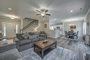 A spacious living room with a grey sofa, a wooden coffee table, and a dining area with a table and chairs. A staircase leads to an upper level.