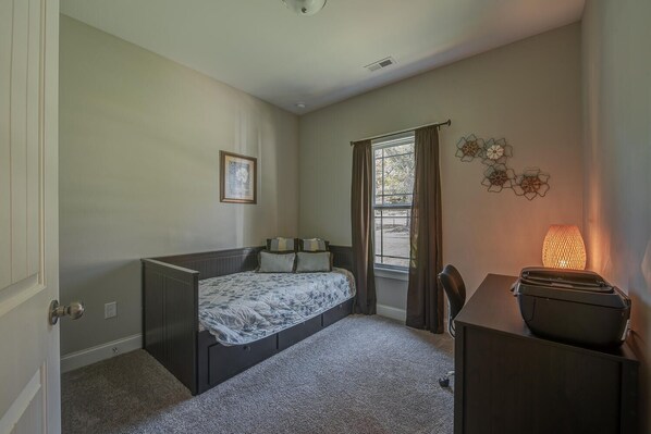 A bedroom with a bed, a desk, a chair, a window with curtains, and a wall-mounted lamp.