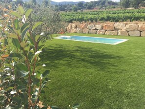 A swimming pool surrounded by a well-maintained lawn, with a stone wall and vineyard in the background. - Villa located in the heart of Provence with private pool on 3 hectares. (Roquevaire)