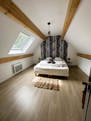 Cozy retreat with a sloped ceiling, wooden beams, and a skylight, featuring a comfortable bed and a colorful abstract wall pattern.