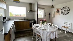 Cocina moderna con comedor, que cuenta con un amplio ventanal, piso de madera y un reloj en la pared.