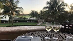 Una mesa con un plato de pasteles, dos copas de vino blanco y un teléfono inteligente en un balcón con vista a un campo de golf.