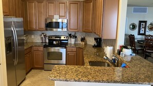 Una cocina con armarios de madera, electrodomésticos de acero inoxidable, encimeras de granito y un comedor con sillas y mesa de madera.