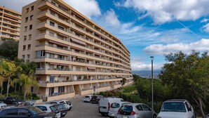 Un hôtel à plusieurs étages doté de balcons, un parking où sont garées différentes voitures, et une vue sur la mer.