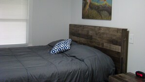 A bedroom with a wooden headboard, a bed with grey bedding, a patterned pillow, a painting on the wall, and a digital clock on the nightstand. - Ft Gibson Lake OK near Sequoyah State Park (Hulbert)
