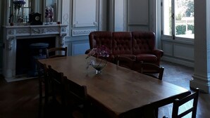 A dining room with a wooden table and chairs, a red upholstered sofa, a chandelier, and a fireplace.
