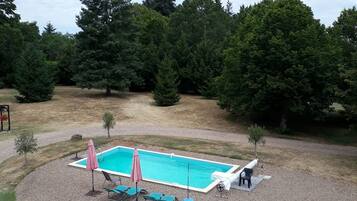 A rectangular swimming pool with a white deck, surrounded by a gravel area. There are lounge chairs and a small umbrella near the pool.